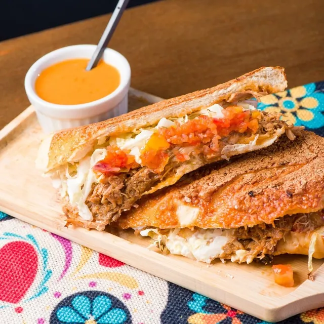Quesadilla dourada na chapa com carne desfiada e vinagrete, ao lado de um potinho de molho