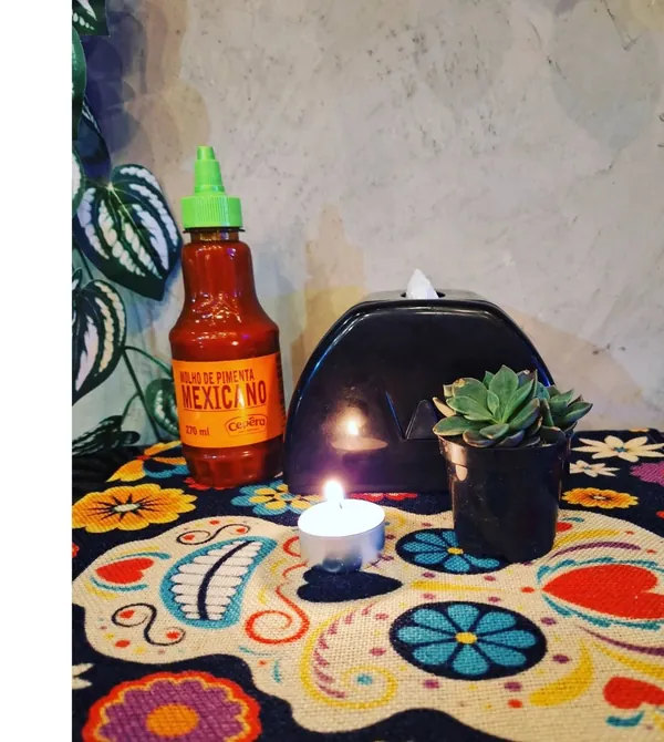 Mesa com molho de pimenta mexicano, vela e suculenta sobre toalha de caveira mexicana
