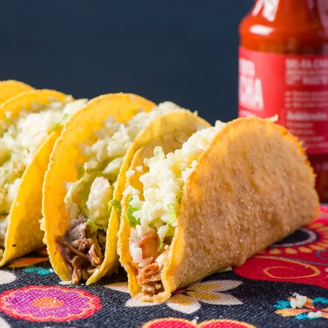 Tacos crocantes recheados com carne e queijo sobre a toalha florida